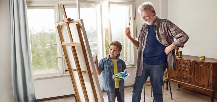 Image of an older man and a boy painting on an easel (not actual patients)