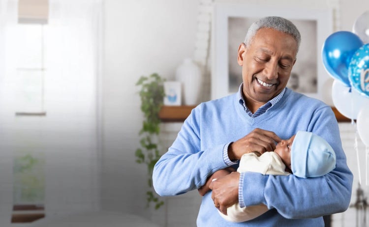 Image of a grandfather holding a baby (not real patients) with blue balloons in background